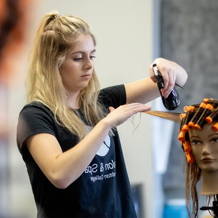 An image of a Lambton College student spraying manequin hair with water,